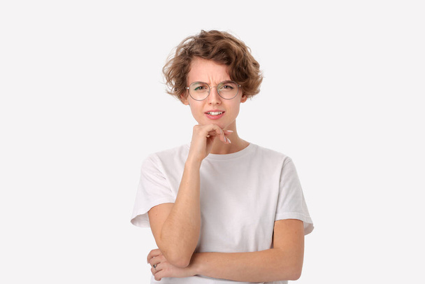 Gedachte jonge vrouw in een wit overhemd en een bril die in een rechter bovenhoek naar de kopieerruimte kijkt, hangt over een witte achtergrond. Concept van het denken - Foto, afbeelding