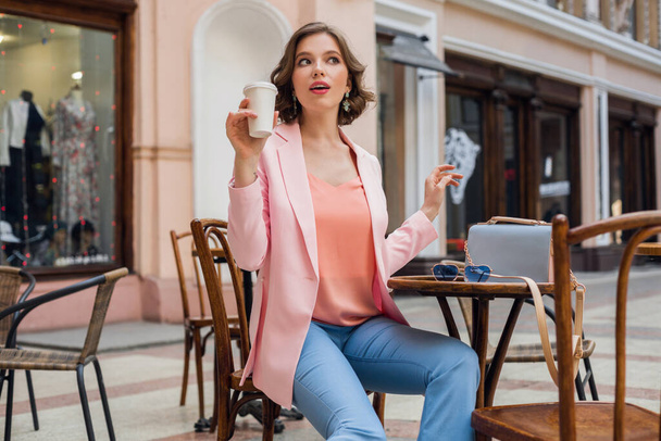 attractive woman in romatic mood smiling in happiness sitting at table wearing pink jacket, stylish apparel, waiting for boyfriend on a date in cafe, drinking cappuccino, exited face expression - 写真・画像