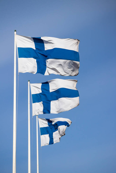 Three finnish national flags on the wind against the blue sky - Photo, Image