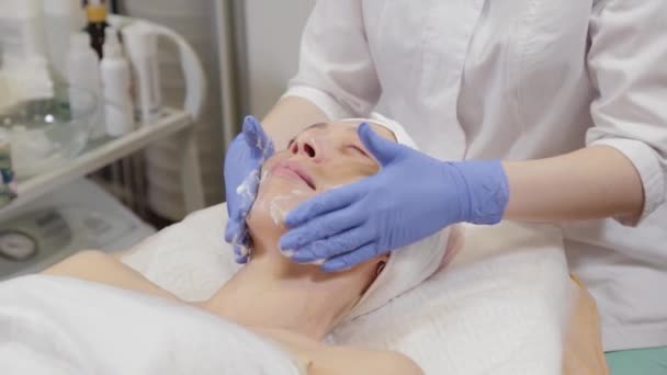 Ammattimainen kosmetologi pesee naisen ja hieroo hänen kasvonsa. - Materiaali, video