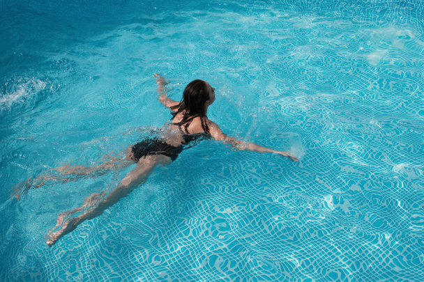 fashion photo of sexy beautiful girl with brunette hair in elegant bikini posing and takes a sunbath in the swimming pool - Valokuva, kuva