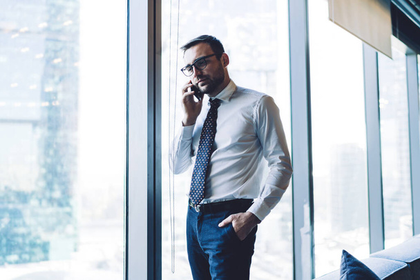 Selbstbewusster männlicher Firmeninhaber ruft Geschäftspartner per Smartphone-Gerät an, um über das Projekt zu kommunizieren, gutaussehender Mann in optischer Brille unterhält sich mit Beratungskollege - Foto, Bild