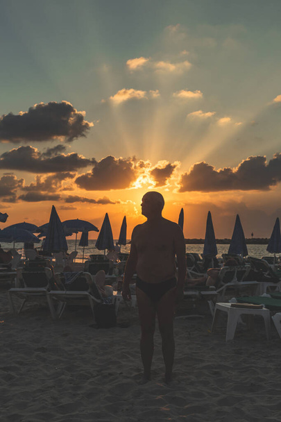 Silueta muže stojícího mezi lehátky na pláži v Tel Avivu večer těsně před západem slunce - Fotografie, Obrázek