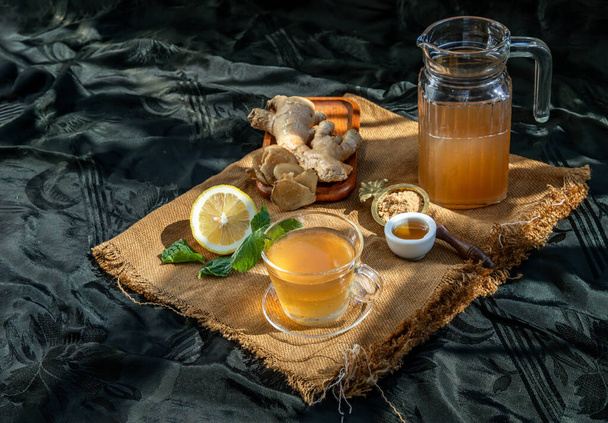 Hot Ginger juice with lemon and mint, root and slices of ginger Served with brown sugar and honey on sackcloth background. Hot ginger juice can helps warming body, Healthy Drink. - Fotó, kép