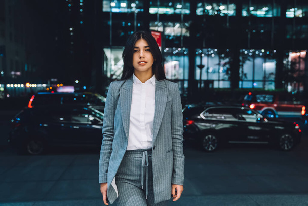 Carefree and pleased ethnic female entrepreneur in elegant suit with loose long black hair looking at camera on blurred background - Фото, зображення