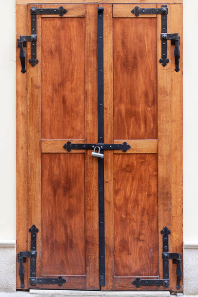 鍛造ヒンジで茶色の木製のドアを粉砕します。南京錠でロックされたヴィンテージドア. - 写真・画像