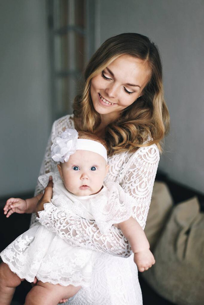 Young mother with daughter on hands in white dresses - Photo, Image