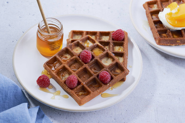 Homemade waffles with honey, raspberry, peaches in syrup in plate on grey surface. Healthy breakfast, brunch concept. Selective focus. Close up. - Foto, Imagem