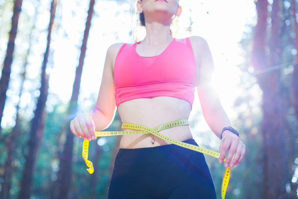 Foto de una joven en forma y saludable midiendo su cintura con una cinta métrica controlando su pérdida de peso mientras entrenaba en el bosque
 - Foto, imagen