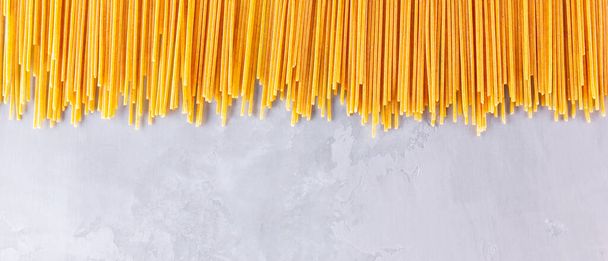 Yellow pasta on a gray background. Spaghetti on cement background. Raw spaghetti bolognese. Food background concept. Top view - Photo, Image