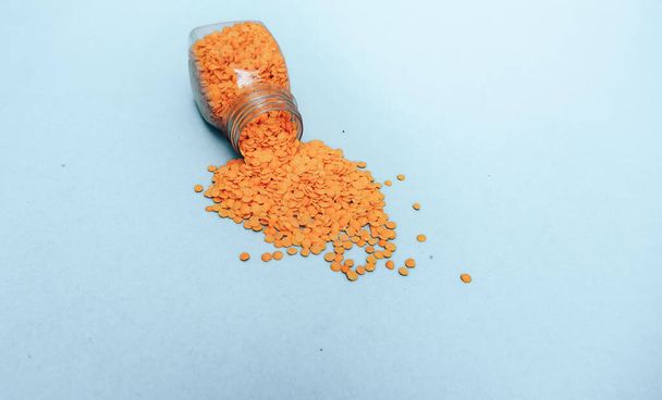 Piccola bottiglia di semi di lenticchia arancione su sfondo blu
.  - Foto, immagini