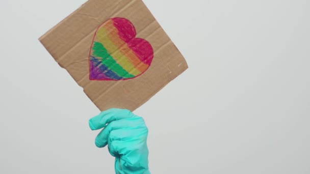 Ημέρα υπερηφάνειας. LGBTQ φιλικό προς το σύστημα υγείας εργαζόμενος κρατώντας χειροποίητα πλακάτ με σημαία ουράνιο τόξο σε σχήμα καρδιάς. ΛΟΑΤΚΙ γιατρός μάχεται στην πρώτη γραμμή κατά του ιού της στέψης. - Πλάνα, βίντεο