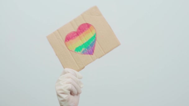 Ημέρα υπερηφάνειας. LGBTQ φιλικό προς το σύστημα υγείας εργαζόμενος κρατώντας χειροποίητα πλακάτ με σημαία ουράνιο τόξο σε σχήμα καρδιάς. ΛΟΑΤΚΙ γιατρός μάχεται στην πρώτη γραμμή κατά του ιού της στέψης. - Πλάνα, βίντεο