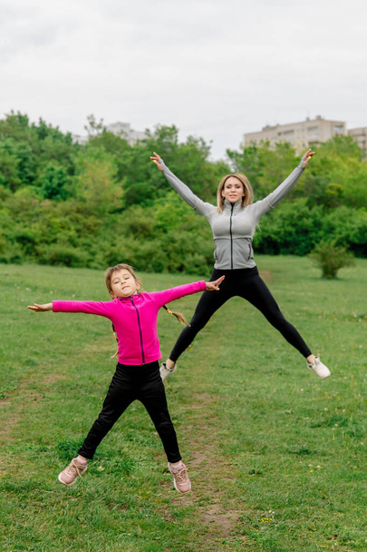 Girl with mom play high jump for a walk in the summer park - Fotoğraf, Görsel
