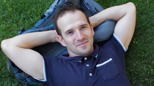 Mladý muž leží na trávě s batohem pod hlavou - Záběry, video