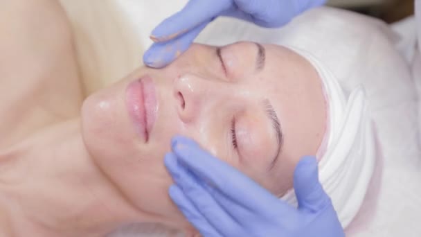 Profesional aplica crema a la cara de una mujer cliente. Cosmetología
. - Imágenes, Vídeo