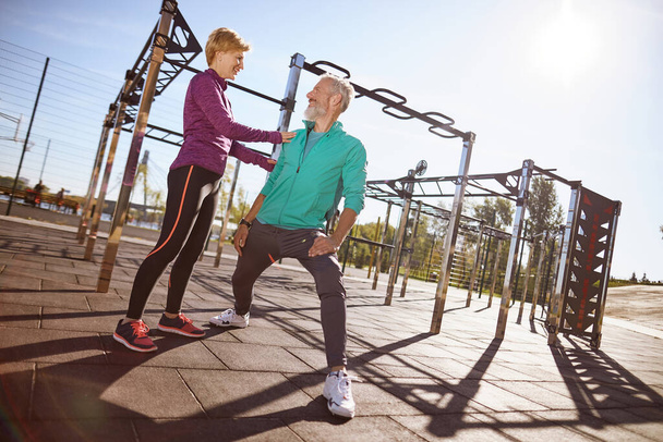Sporty mature woman talking something to her husband while doing sport together outdoors. Happy mature couple in sportswear exercising together in the early morning at the stadium - Photo, Image