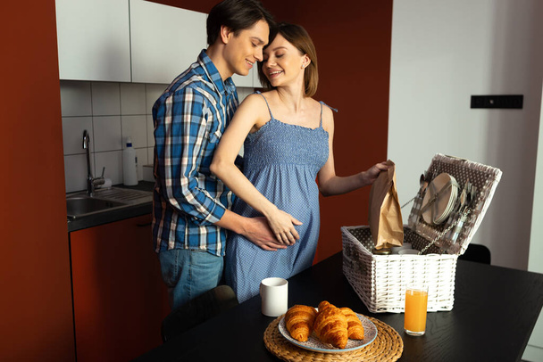 Loving man and pregnant woman cuddling in kitchen - Foto, imagen