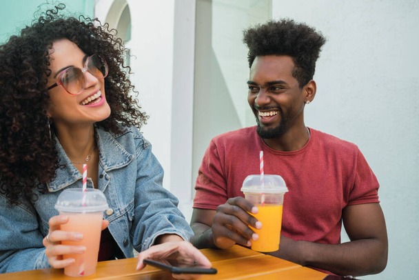 Portrait of two Afro friends having fun together and enjoying good time while drinking fresh fruit juice outdoors at cafeteria. - Foto, Bild
