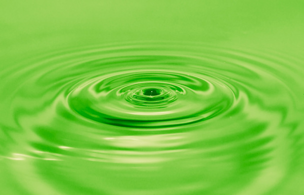 A drop of water falls into the green water - Foto, afbeelding