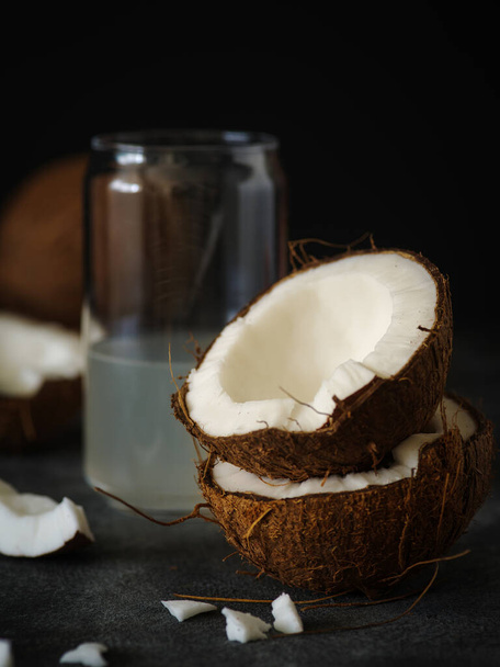 Kokosové půlky na tmavém pozadí se sklenicí kokosové vody - Fotografie, Obrázek
