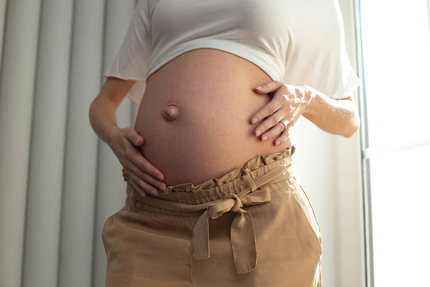Schwangere Frau posiert und legt Hände auf den Bauch - Foto, Bild