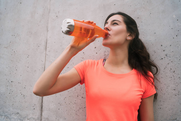Portrait of an athletic woman drinking water after training against grey background. Sport and health lifestyle. - Foto, Bild