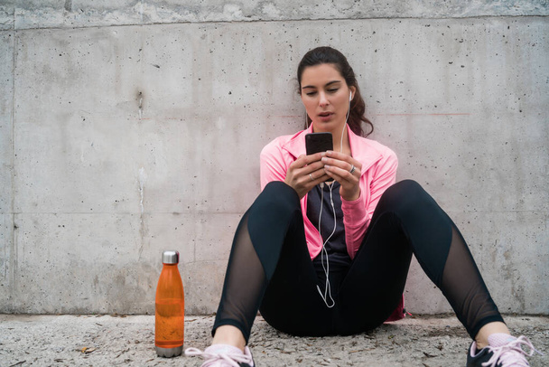 Portrait of an athletic woman using her mobile phone on a break from training against grey background. Sport and health lifestyle. - Valokuva, kuva