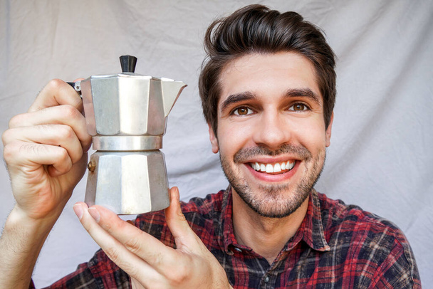 Portrait d'un jeune homme joyeux avec un sourire heureux tout en tenant un pot de moka brillant avec un café dans une chemise
 - Photo, image
