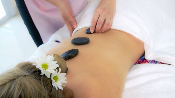 Woman getting hot stone massage treatment by professional beautician therapist in spa salon. Luxury wellness, back stress relief and rejuvenation concept. - Foto, imagen