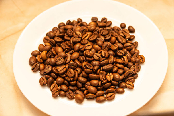 焙煎されたコーヒー粒は白いプレートの上にあります。コーヒーを飲む. - 写真・画像