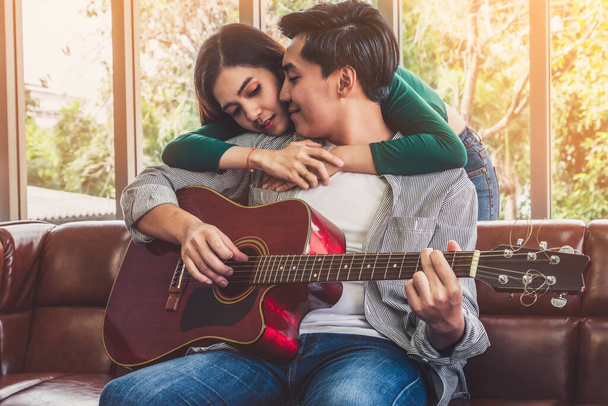 Młoda azjatycka para gra na gitarze i śpiewa piosenkę w salonie w domu razem. Koncepcja muzyki i stylu życia. - Zdjęcie, obraz