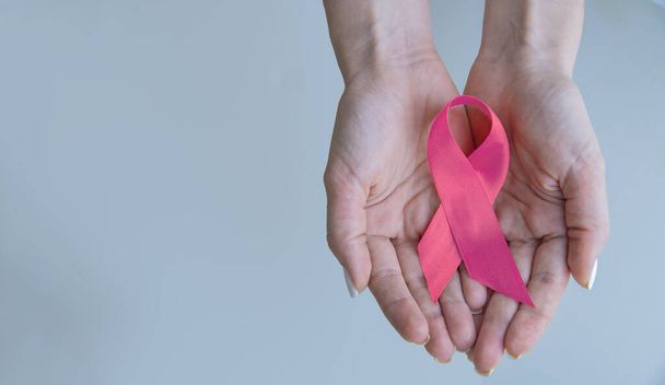 Koncepcja opieki zdrowotnej i medycyny - dziewczęce dłonie trzymające różową wstążkę świadomości raka piersi. - Zdjęcie, obraz