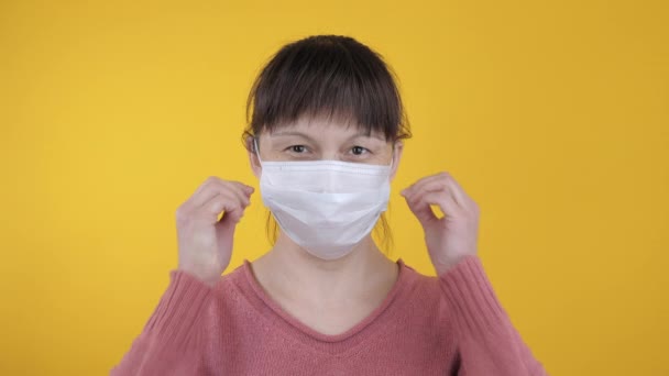 Joyful woman takes off a medical mask on a yellow background - Felvétel, videó