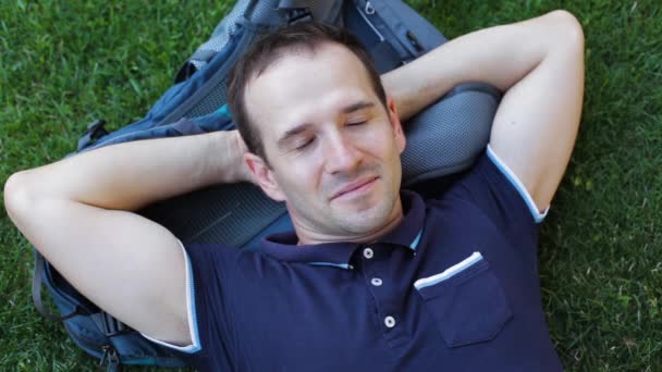 Een jonge man ligt op het gras met een rugzak onder zijn hoofd - Video