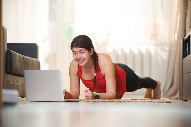 Las mujeres en ropa de entrenamiento atlético está haciendo un ejercicio de tablón mientras usa video tutoriales
. - Foto, imagen