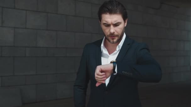 Besorgter Geschäftsmann kontrolliert Zeit auf Armbanduhr in moderner Stadt - Filmmaterial, Video