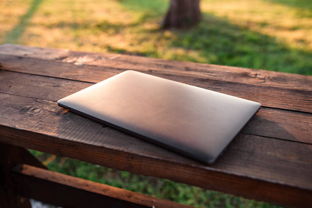 Μονός φορητός υπολογιστής σε ξύλινο τραπέζι. Laptop που βρίσκεται σε ένα ξύλινο τραπέζι πίσω από το οποίο είναι το ηλιοβασίλεμα. Το λάπτοπ. Ελεύθερος χώρος για το κείμενο σας. - Φωτογραφία, εικόνα