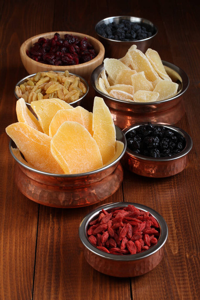 Kandírozott gyömbérgyökér szeletek, szárított mangó gyümölcsök, szárított áfonya és goji bogyók, szárított áfonya, arany és kék mazsola kis tálakban egy fa asztalon. Közelkép - Fotó, kép