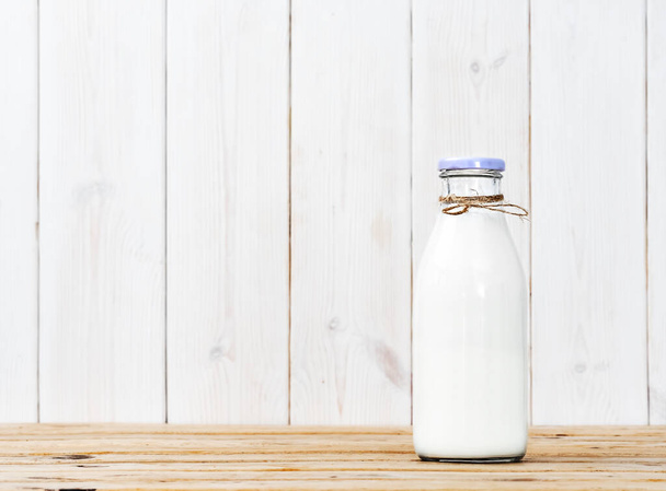 Fles melk op een houten vintage tafel, witte houten ondergrond met kopieerruimte. Verse melk, herbruikbaar glaswerk - Foto, afbeelding