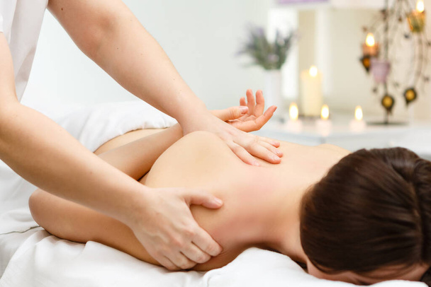 A beautiful girl lies on a massage table and she gets a massage that she enjoys in the massage room - Φωτογραφία, εικόνα
