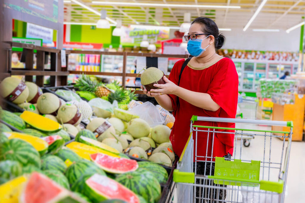 Frau mit Schutzmaske beim Einkaufen während der Pandemie. Notfall zum Einkaufen, Nahrungsmittel und Vorräte knapp. Schutzmaßnahmen zur Zeit der Epidemie. Vorbereitung auf eine Pandemie-Quarantäne - Foto, Bild