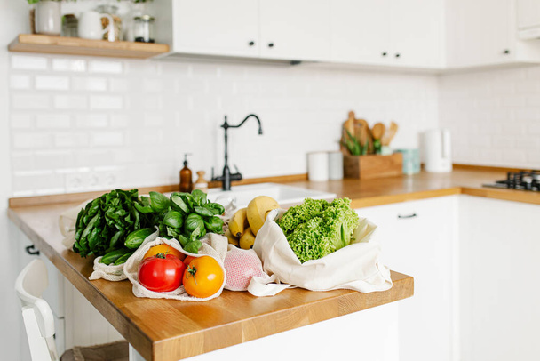 Fresh vegetables and fruits in eco cotton reusable bags on wooden table in the kitchen. zero waste shopping concept. Sustainable living - Foto, imagen