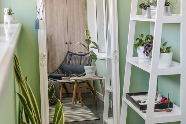 Interior de acogedor balcón con paredes verdes, sala de estar con alfombra, sillón y dos mesas de café
 - Foto, Imagen