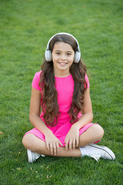 Educational podcast. Kid girl enjoy music green grass meadow. Pleasant time. Child headphones listen music. Girl headphones listening music. My summer playlist. Listen music while relaxing outdoors - Φωτογραφία, εικόνα