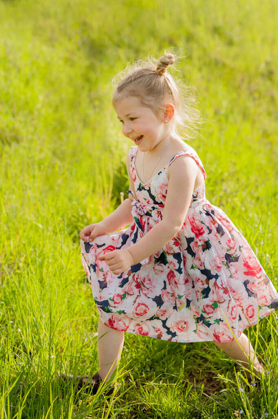 Egy kislány nyári ruhában, copfokkal a zöld mezőn, meleg napsugarakkal. - Fotó, kép