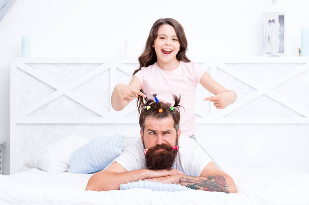 Relaxing in bedroom. Stay home and have fun. Family leisure concept. Girl making hairdo for dad. Quarantine with children. Happy family. Pajamas party. Happy childhood. Affection and support - Photo, image