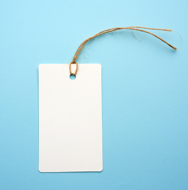 Blank white paper tag with white rope on a blue background. Price tag, gift, for writing address - Photo, Image