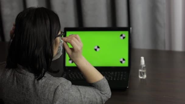 Nő eltávolítja orvosi maszk, hogy fertőtlenítő és használja közelében laptop zöld képernyővel - Felvétel, videó