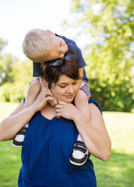 Mujer llevando hijo en hombros en parque
 - Foto, Imagen